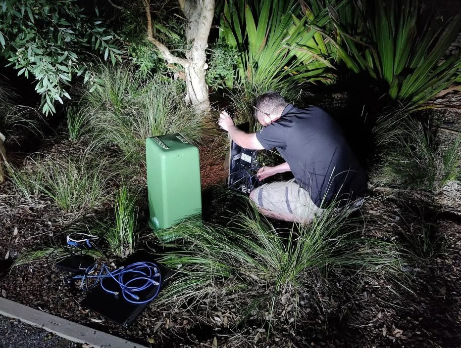 ACS technician working on an outdoor network cabinet at night